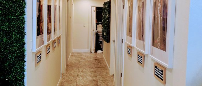 Bright, welcoming hallway at Balance Skin & Wellness in San Antonio, lined with framed artwork and greenery for a calming first impression.