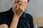 Adult woman using cotton pad and toner for skincare routine indoors.