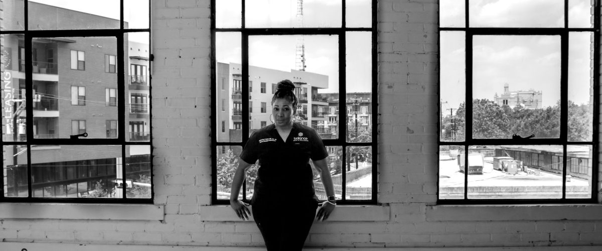 Rashonda Davis – Visionary Founder of Balance Skin & Wellness Black and white portrait of Rashonda Davis standing confidently in front of large windows, representing leadership at Balance Skin & Wellness.